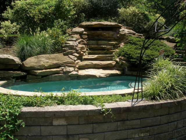 Custom landscape design, natural stone outdoor spa with waterfall. Spa is set inside landscaped bed surrounded by stone retaining wall